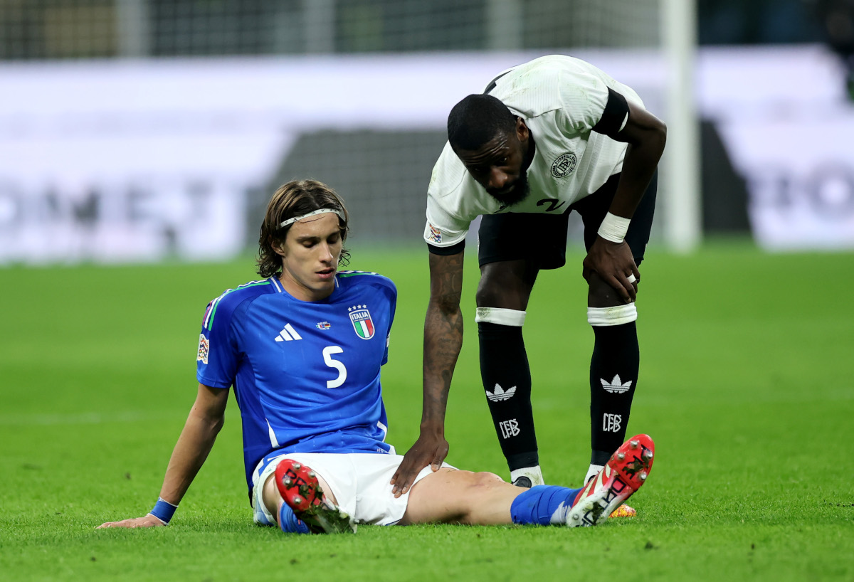 MILAN, ITALY - MARCH 20: Riccardo Calafiori of Italy goes down with an injury and is checked on by Antonio Ruediger of Germany during the UEFA Nations League quarterfinal leg one match between Italy and Germany at Stadio San Siro on March 20, 2025 in Milan, Italy. (Photo by Alex Grimm/Getty Images)